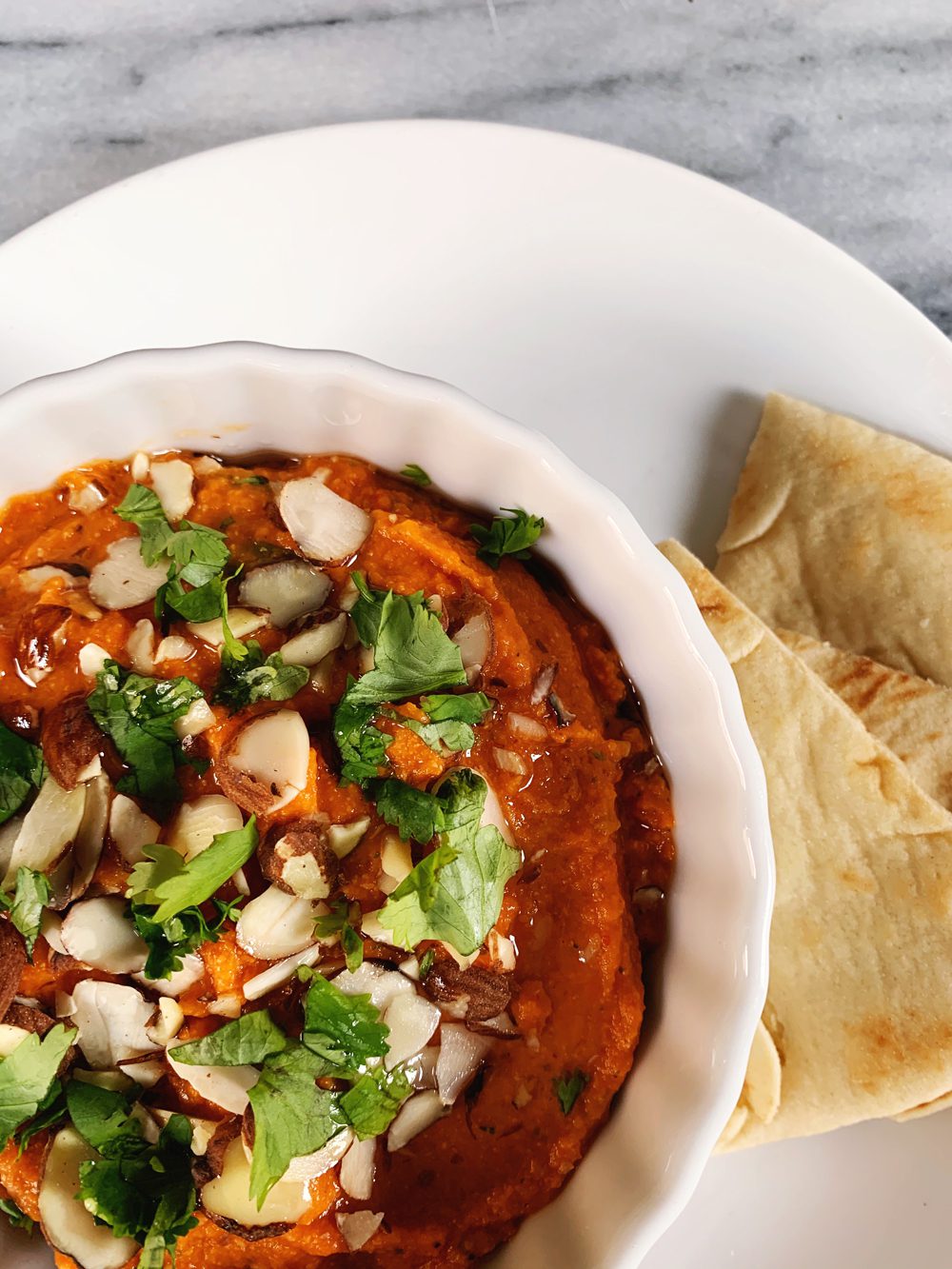 Close up of Roasted Red Pepper Hummus with Harissa, sliced almonds, and cilantro