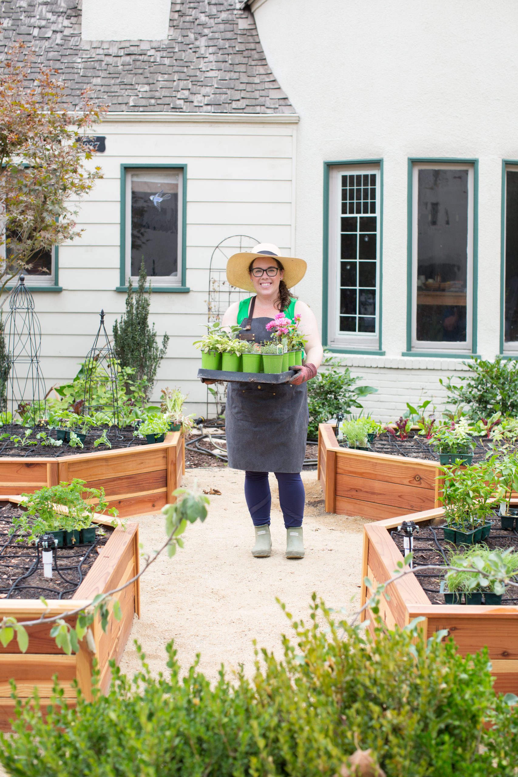 Ashley Irene in the Heirloom Potager Showcase Garden holding a flat of plants with her signature garden hat