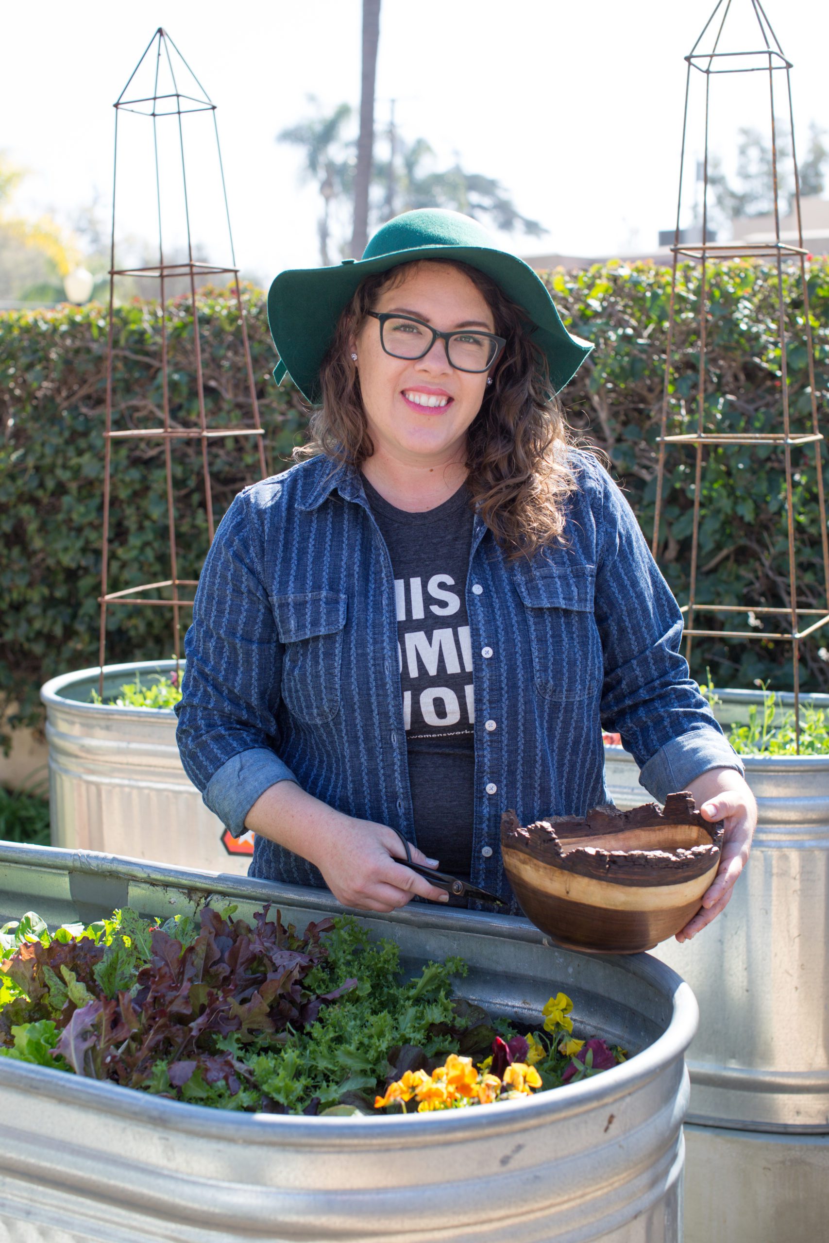 Ashley Irene, founder of Heirloom Potager in a clients culinary garden holding a bowl of garden fresh produce