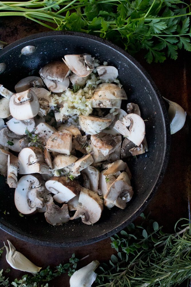 Raw button and crimini mushrooms with garlic and herbs in a sautee pan