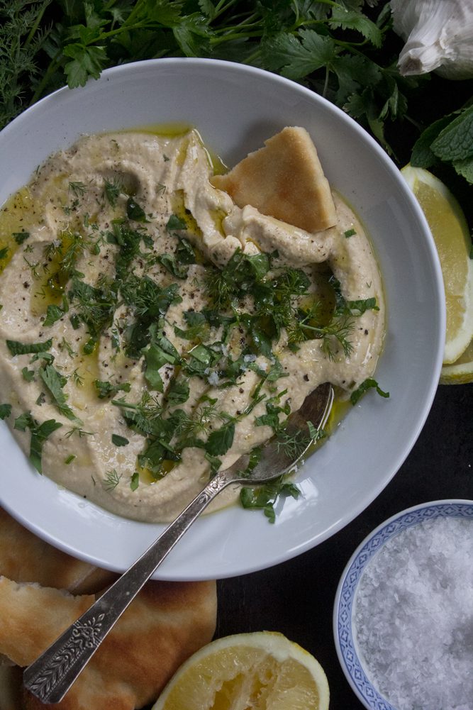 Plate of traditional hummus garnished with fresh dill, cilantro, parsley, and mint with a drizzle of extra virgin olive oil, sea salt, and fresh cracked pepper