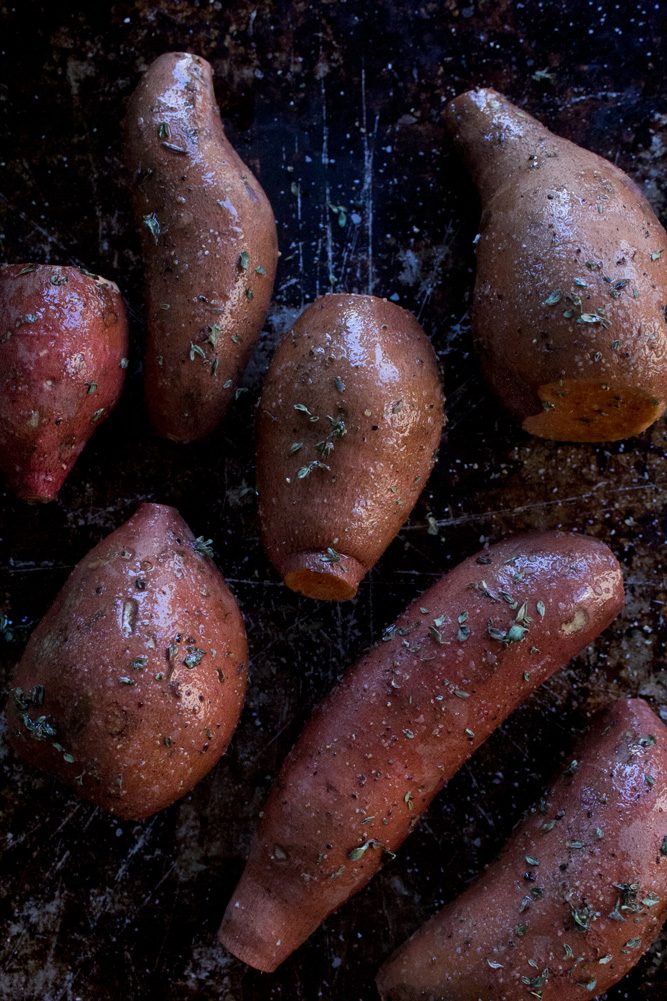 Red skinned sweet potatoes on a baking sheet sprinkled with fresh thyme, rosemary, sea salt and fresh pepper