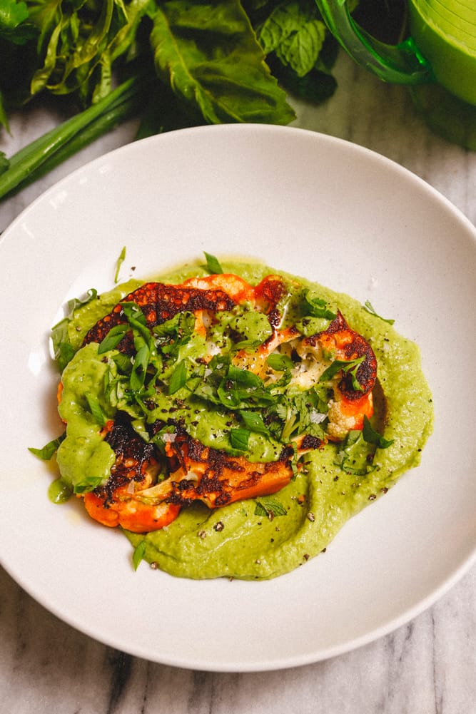 Spicy cauliflower steak served with fresh tender herbs and green goddess spring hummus.