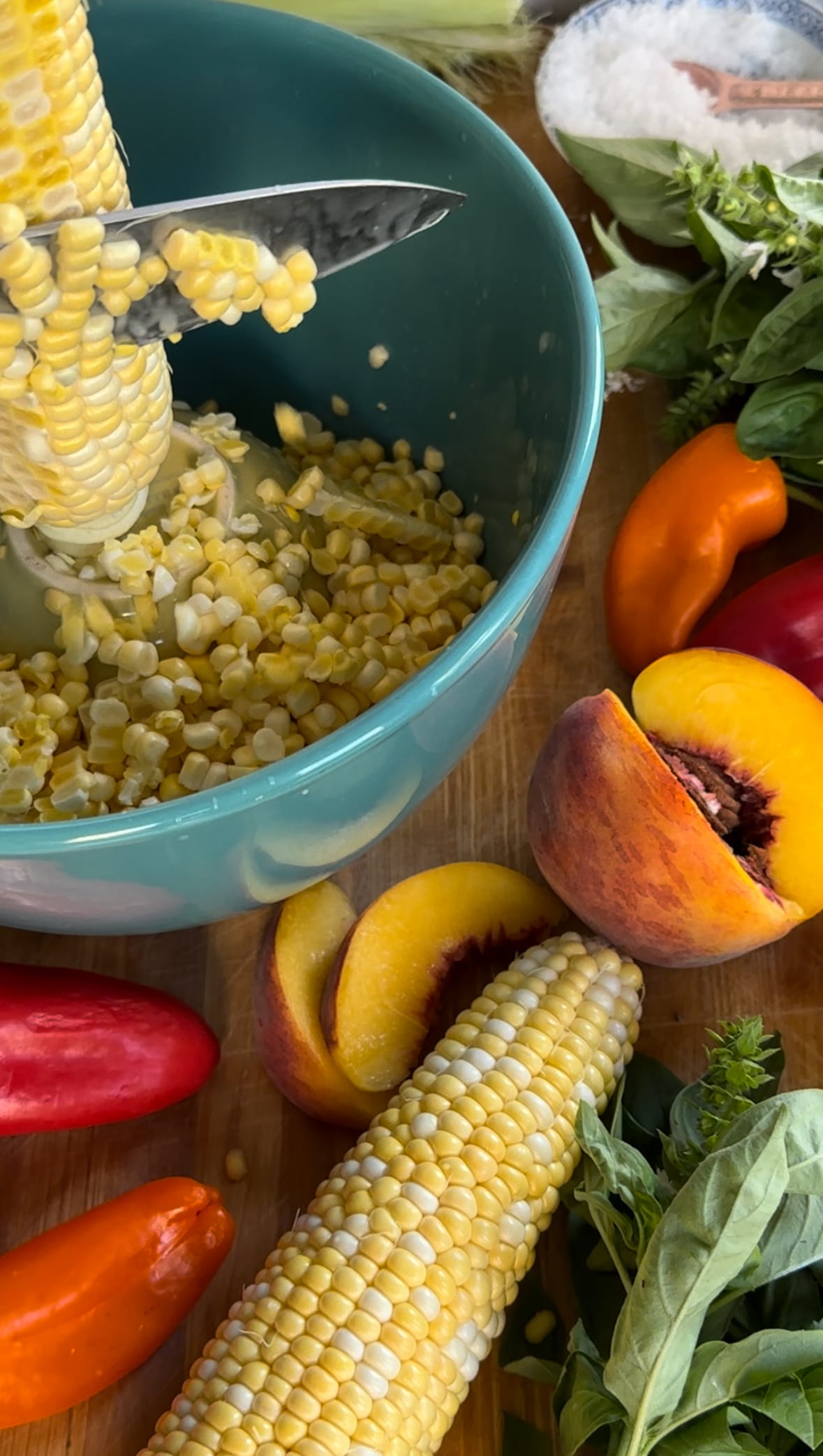 Cutting fresh sweet corn into a bowl for Summer corn, pepper, and peach salad with argula