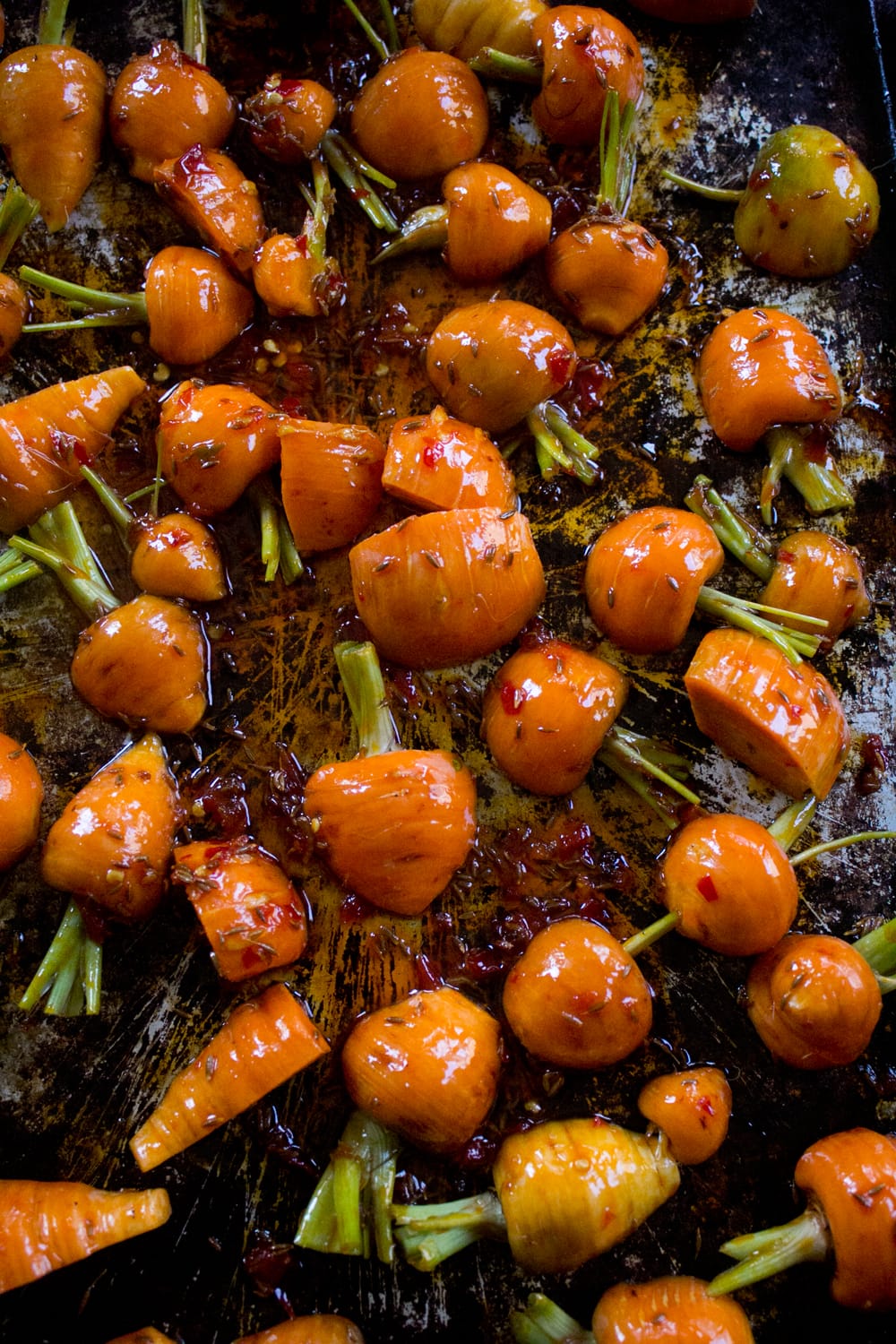 Garden-fresh carrots trimmed of their greens and sliced, dressed in a harissa, honey, and cumin seed marinade before roasting in the oven.