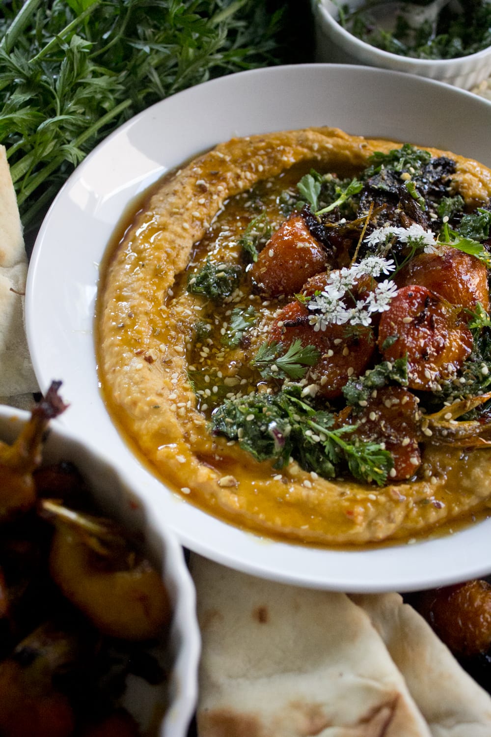 Plated dukkah and carrot hummus with zhoug - sweet, garden fresh carrots roasted with harissa, honey, and cumin seeds added to hummus and dressed with addiitonal roasted carrots, dukkah, zhoug, cilantro leaves + flowers, and drizzled with honey.