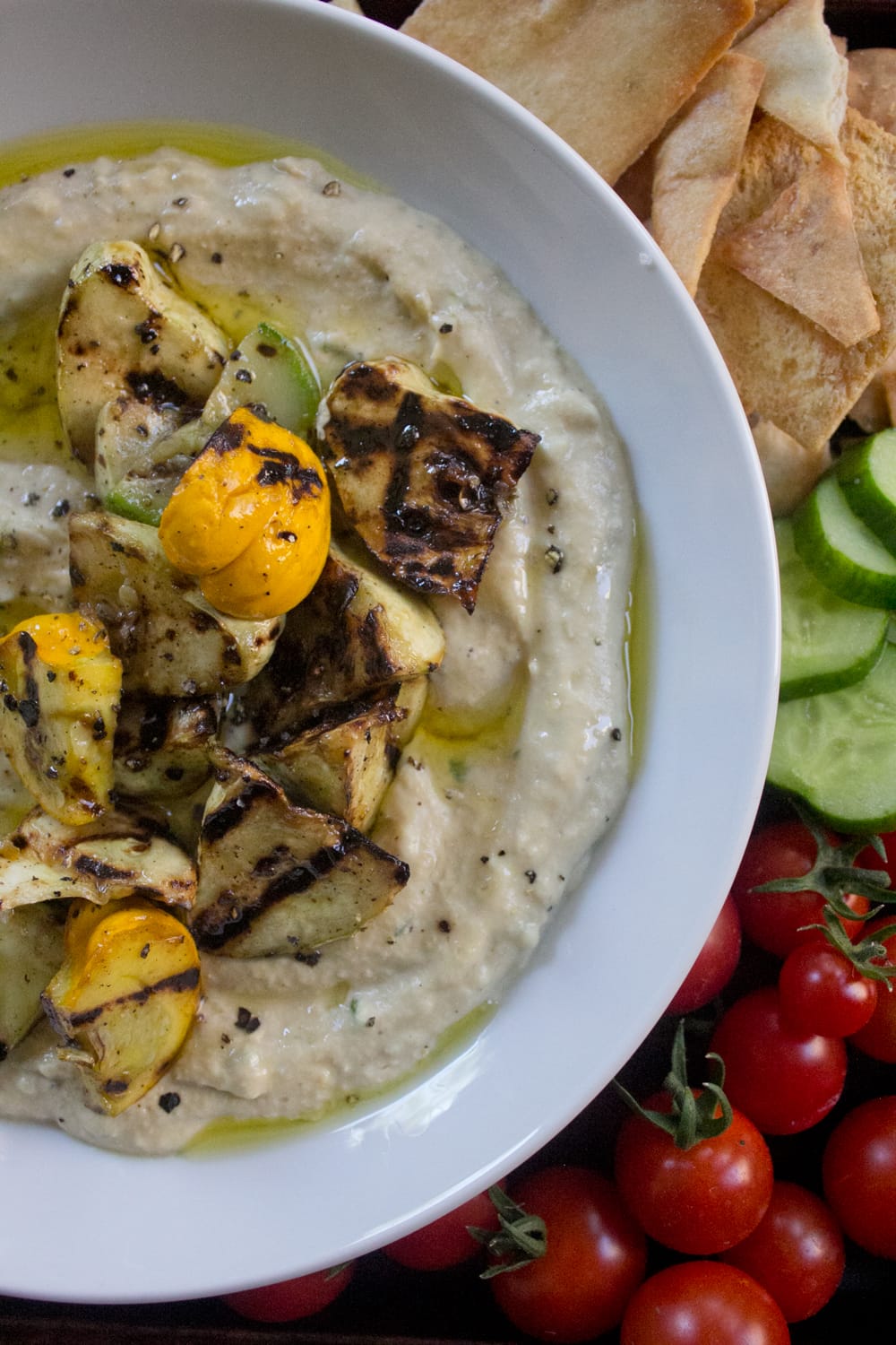 Grilled Summer Squash Hummus plated with cucumber slices, garden-fresh tomatoes, and crispy pita chips